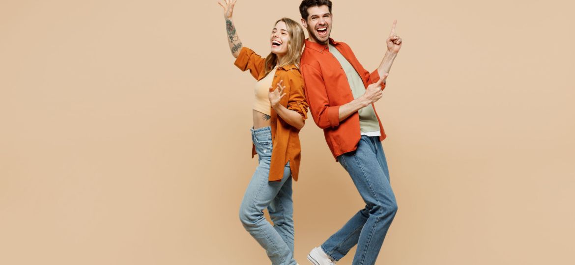 Full body fun young couple two friends family man woman wear casual clothes point index finger aside on area waving hand together isolated on pastel plain light beige color background studio portrait.
