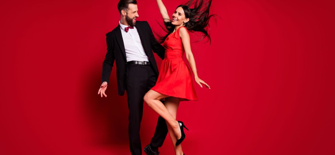 Full size profile photo of optimistic funky couple dance wear vivid dress black suit isolated on red color background